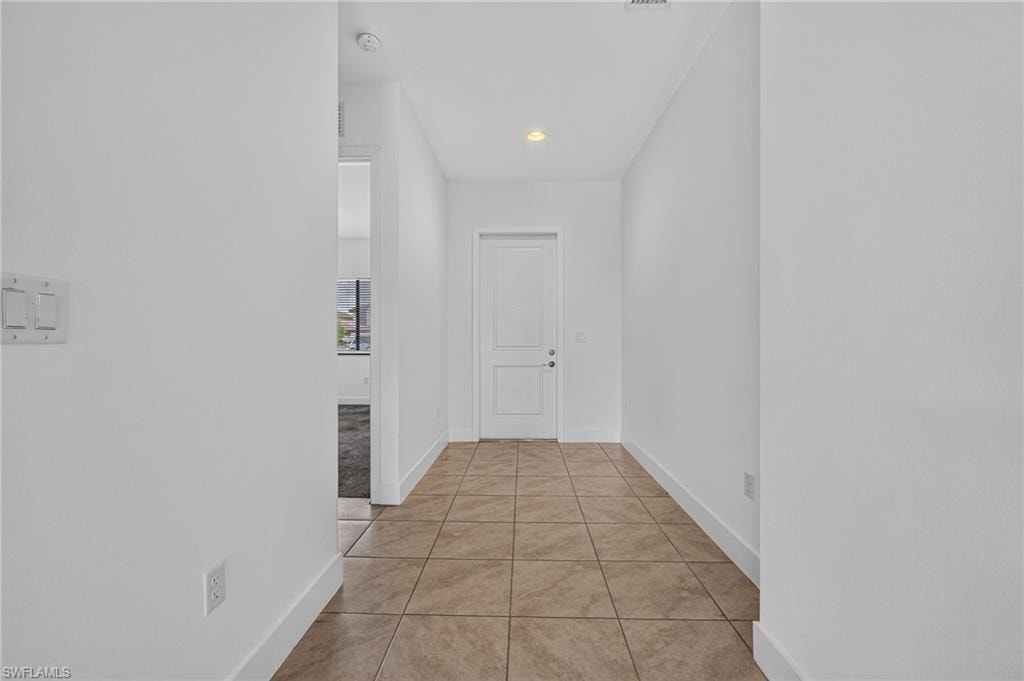 Tile flooring with an inset ceiling light fixture, white interior door, and white wall finishes