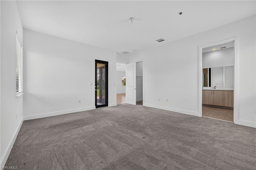 Spacious room featuring gray carpet, white walls, a large window with blinds, and a glass-paneled door