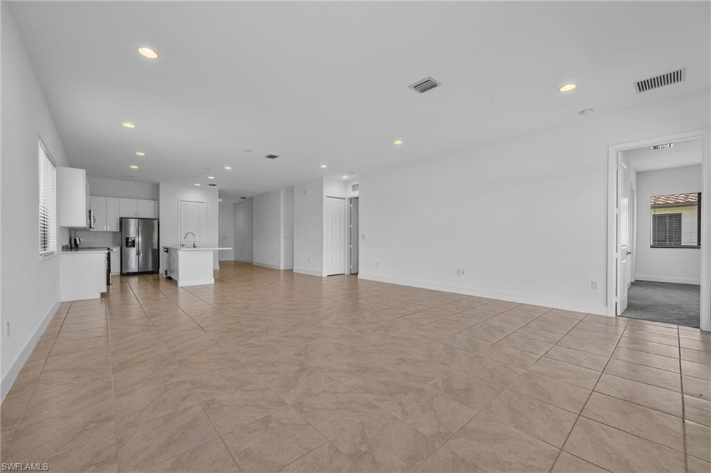 Open-concept living space with large format tile flooring, recessed lighting, and a kitchen featuring white cabinetry and stainless-steel appliances