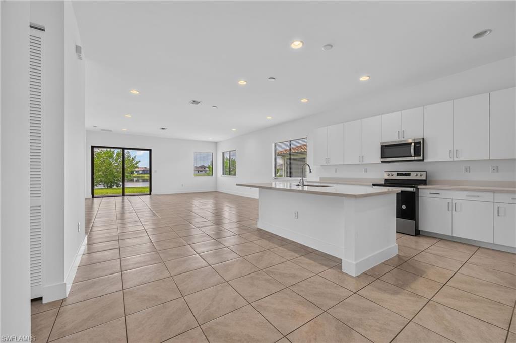 Open-concept living area featuring a kitchen island with sink, white cabinetry, integrated stainless steel appliances, and tile flooring
