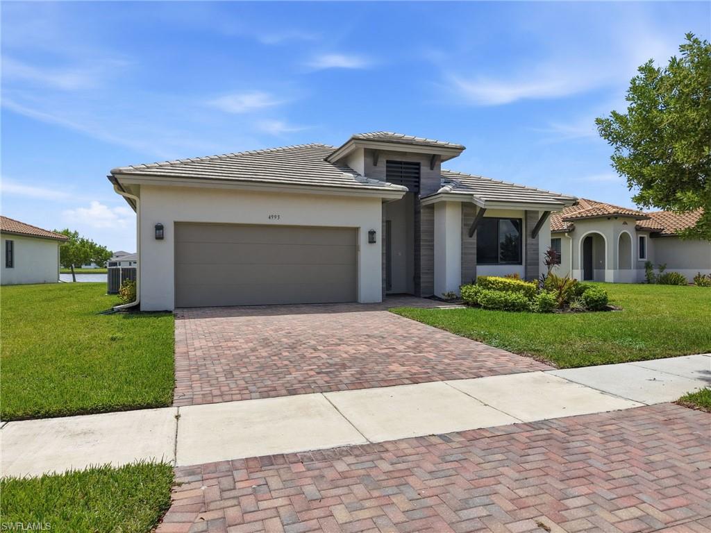 Contemporary stucco exterior with a tile roof, brick paver driveway, and an integrated garage