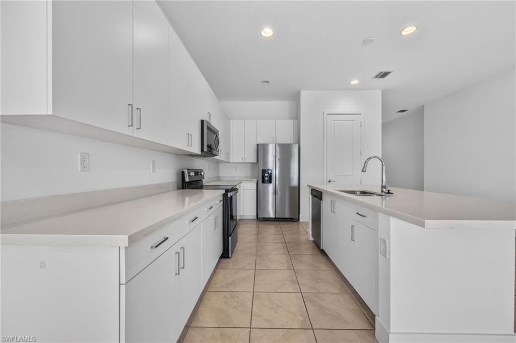 White cabinetry with brushed nickel hardware, stainless steel appliances, light-toned countertops, and recessed lighting