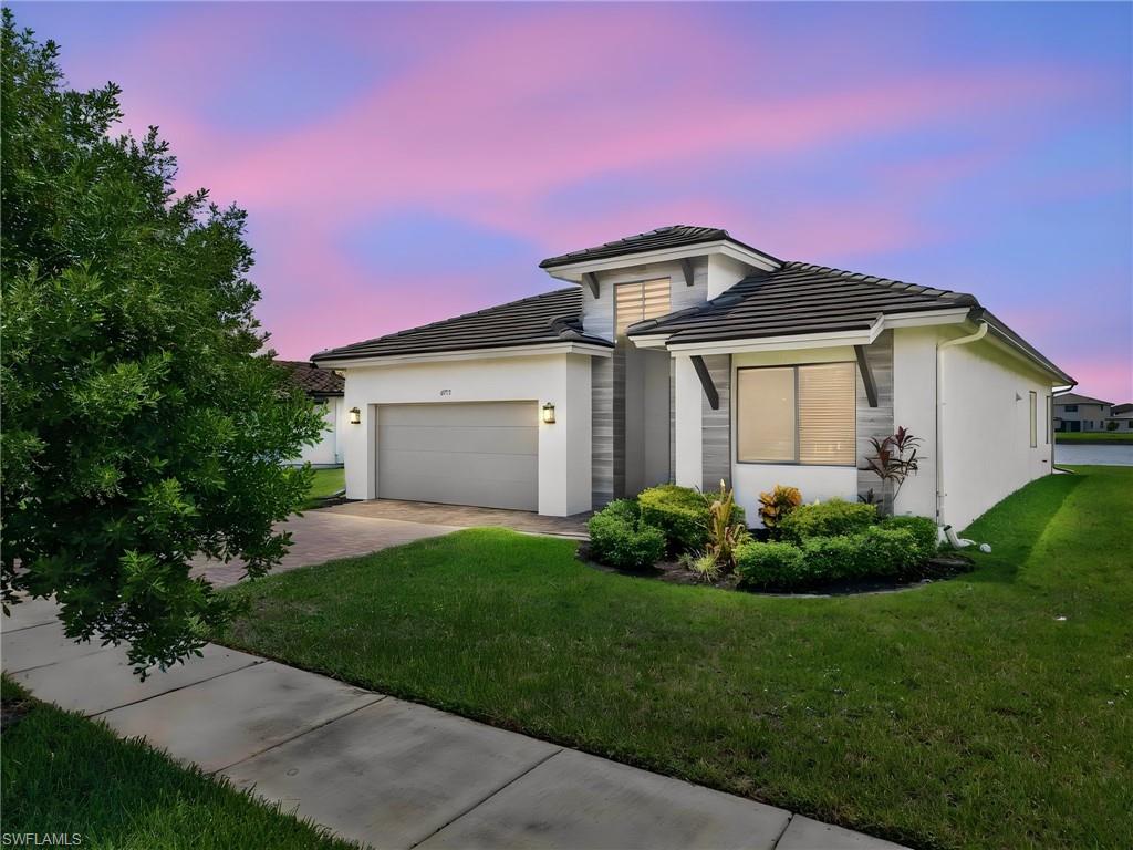 Modern exterior with tile roofing, two-car garage, paver driveway, established landscaping, and a waterside location