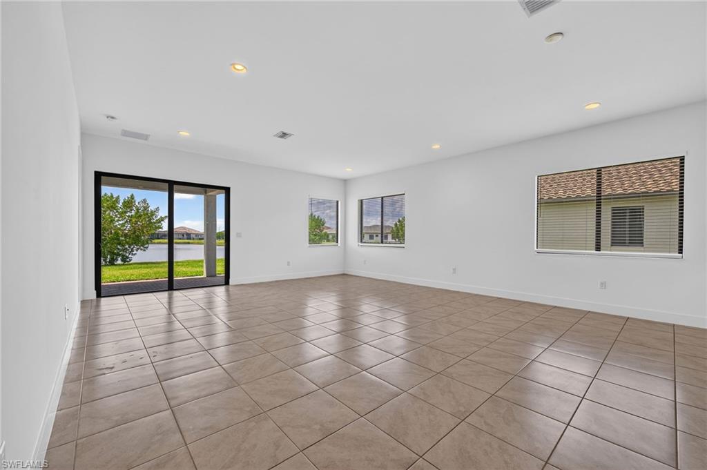 Spacious room with neutral tile flooring, multiple windows, recessed lighting, and sliding glass doors opening to an outdoor area