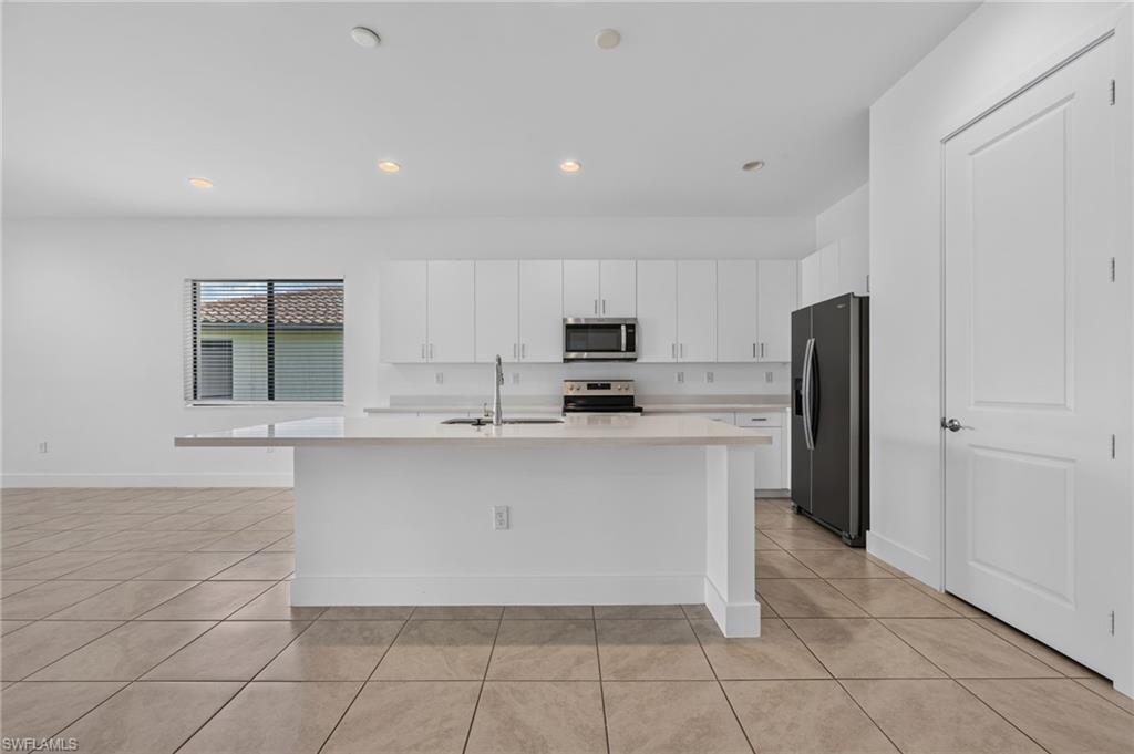 Modern kitchen featuring a large center island, white cabinetry, integrated stainless steel appliances, and tile flooring