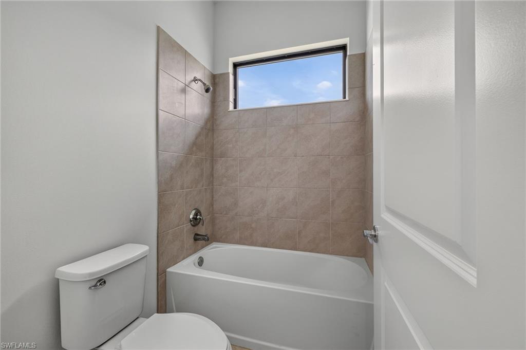 Porcelain tub with a tiled surround, chrome shower fixtures, and a high privacy window