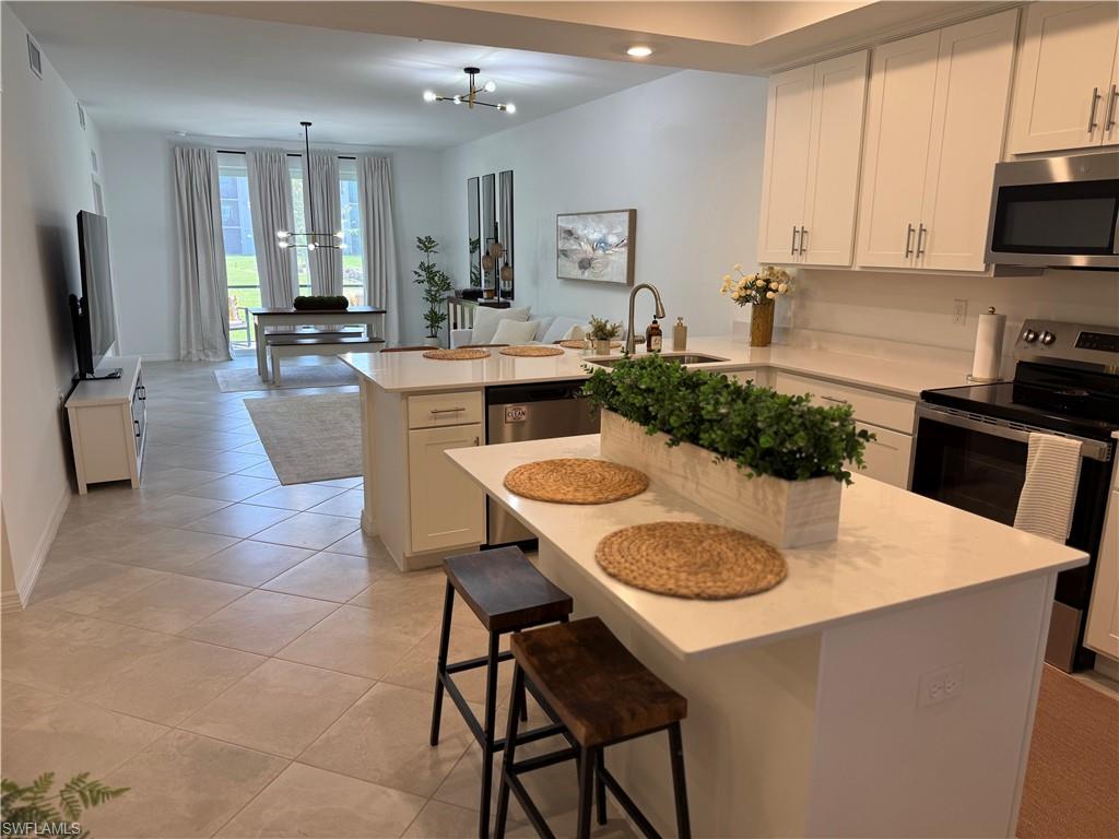 Open-concept living area with tile flooring, white shaker cabinetry, stainless steel appliances, and light-toned countertops