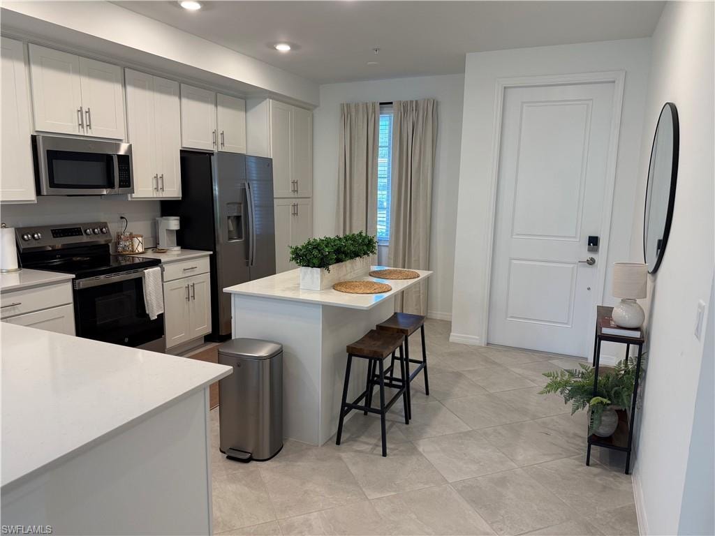 Kitchen featuring white shaker cabinetry, stainless steel appliances, a center island with countertop seating, and light-toned tile flooring