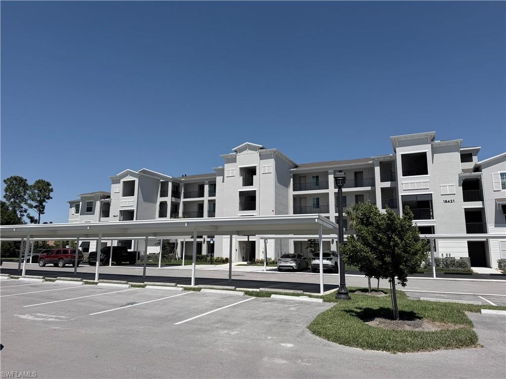 Multi-story building featuring balconies, carports, and an expansive paved parking area