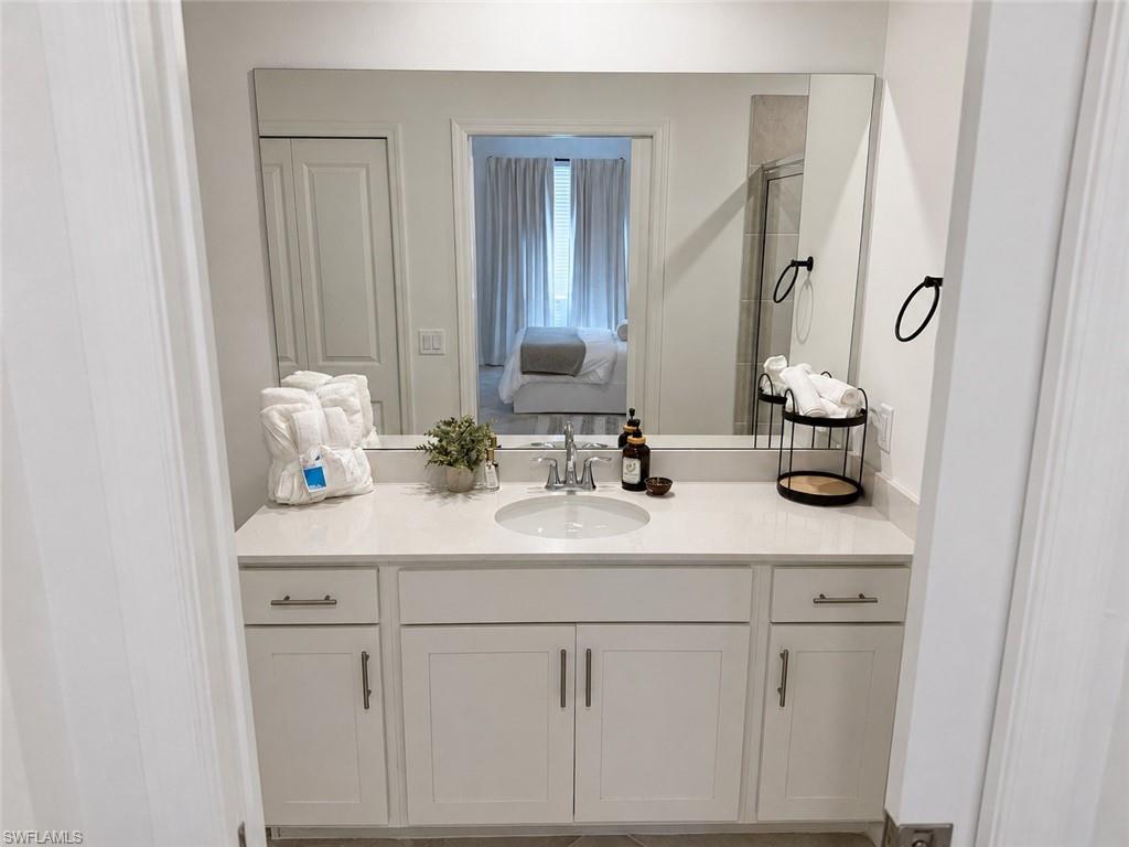 White vanity with a single basin sink, light-toned countertop, and rectangular mirror