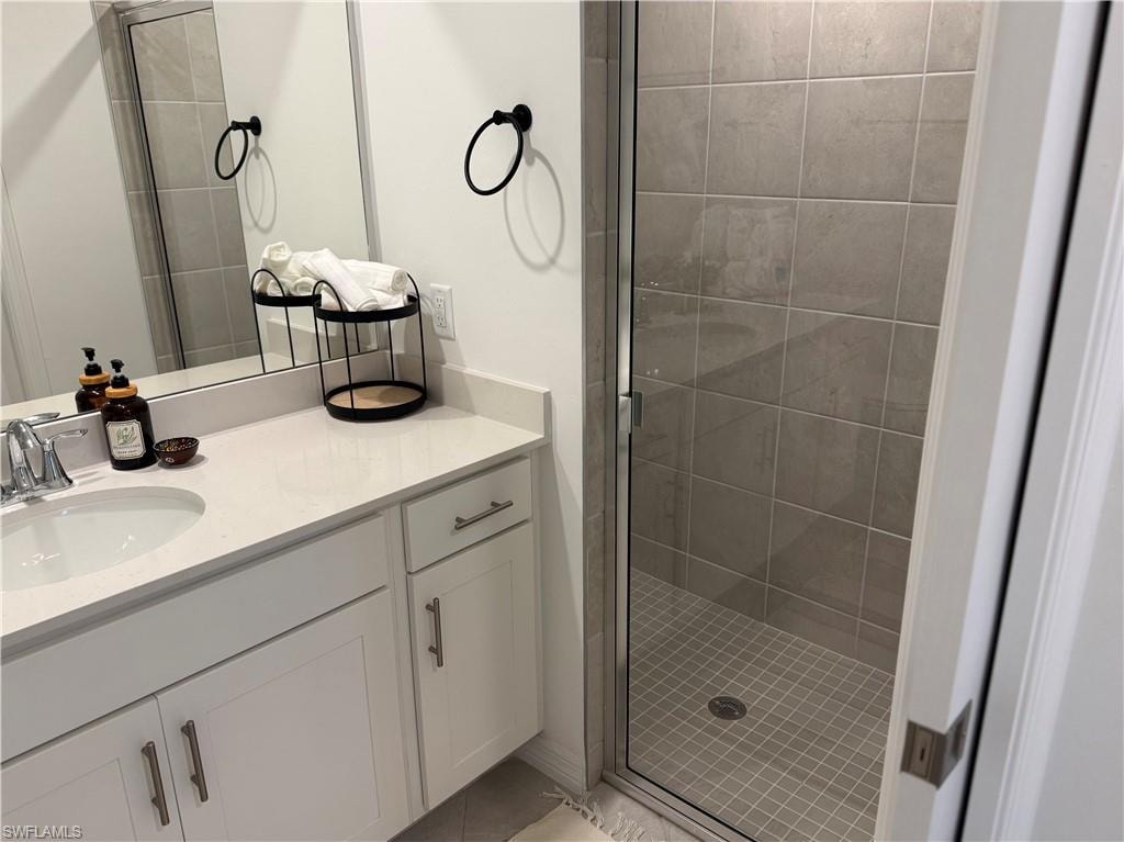 Quartz countertop vanity with an undermount sink, brushed nickel faucet, white cabinetry, and a frameless shower enclosure featuring large-format wall tiles and small-format floor tiles