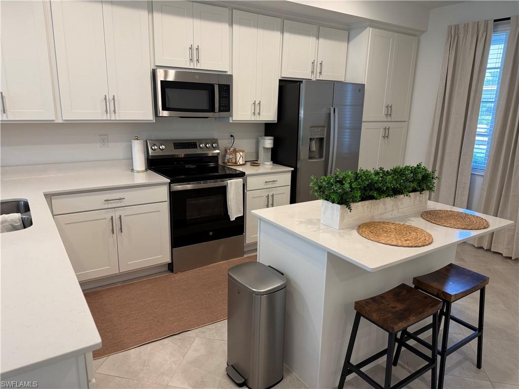 White shaker cabinetry, stainless steel appliances, white countertops, kitchen island, and tile flooring
