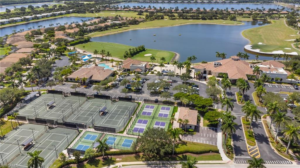 Extensive recreational facilities featuring multiple tennis and pickleball courts, a clubhouse with a barrel-tile roof, and a large swimming pool, all situated alongside a golf course and a significant body of water