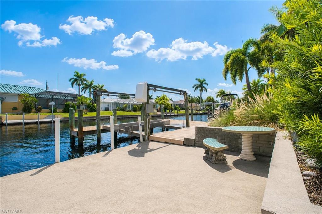 Concrete patio with built-in planter, lush landscaping, and a waterfront boat dock featuring a boat lift
