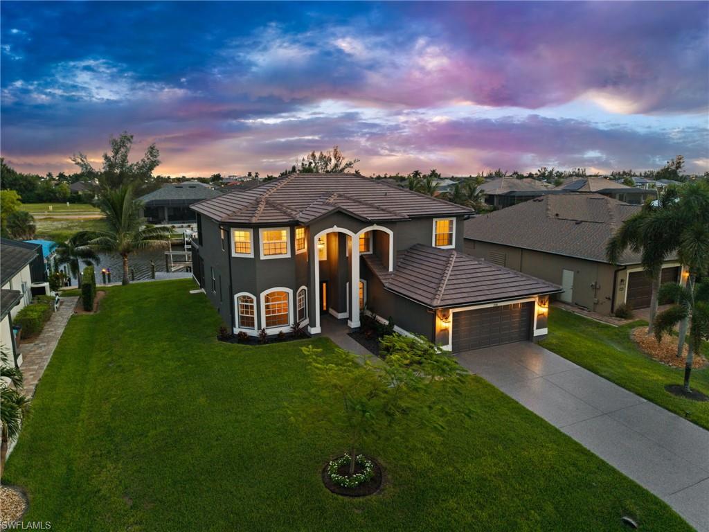 Angled exterior view emphasizes the tall covered entry, arched architectural details, attached garage, and broad lawn. The home's distinctive two-story design creates strong curb presence in this waterfront Cape Coral neighborhood.