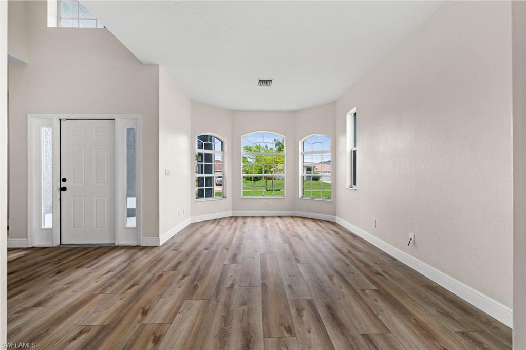 Spacious front living area features wood-look flooring, multiple arched windows, and abundant natural light. The flexible room can accommodate formal living, dining, sitting, or other uses depending on the buyer's needs.
