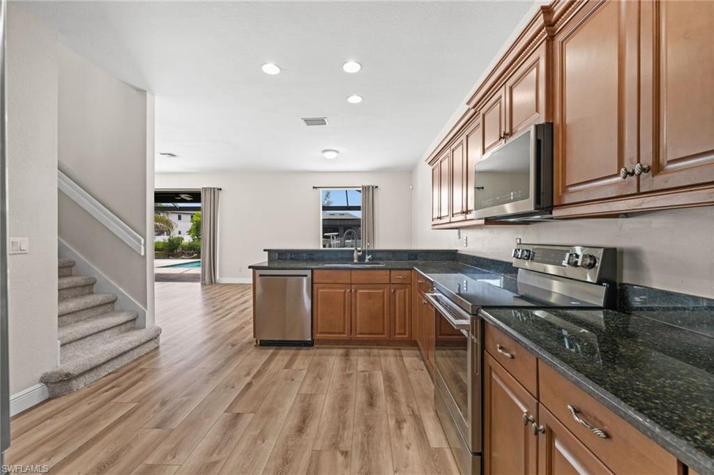 From the kitchen, sightlines extend toward the main living area and screened pool, keeping cooking and entertaining connected. Wood cabinetry, black granite countertops, stainless appliances, and recessed lighting complete the space.