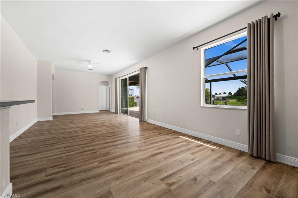 Main living area features wood-look flooring, a ceiling fan, large window, and direct access to the screened pool and lanai. Natural light and outdoor views strengthen the home's indoor-outdoor connection.