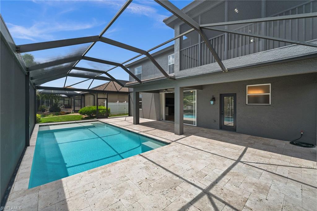 Bright daytime view of the screened pool highlights the generous swimming area, sun shelf, surrounding deck, and rear two-story elevation. Direct access from the interior makes this outdoor space convenient for everyday Southwest Florida living.