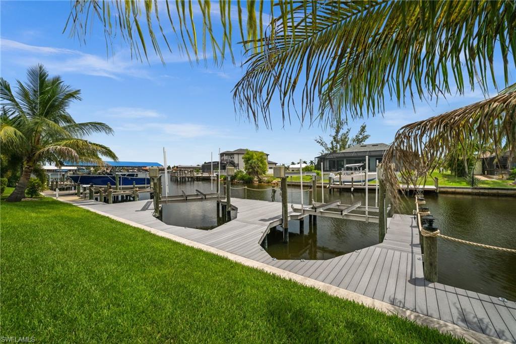 Tropical palms frame the private dock and canal, creating a relaxed waterfront setting directly behind the home. The dock configuration provides a substantial area for boating access and enjoyment of the water.