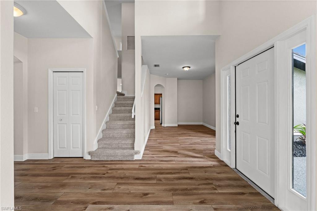 Bright entry view highlights the open staircase, tall ceiling, wood-look flooring, and easy flow into surrounding living areas. The property updates document a full interior paint refresh to the walls and ceilings.