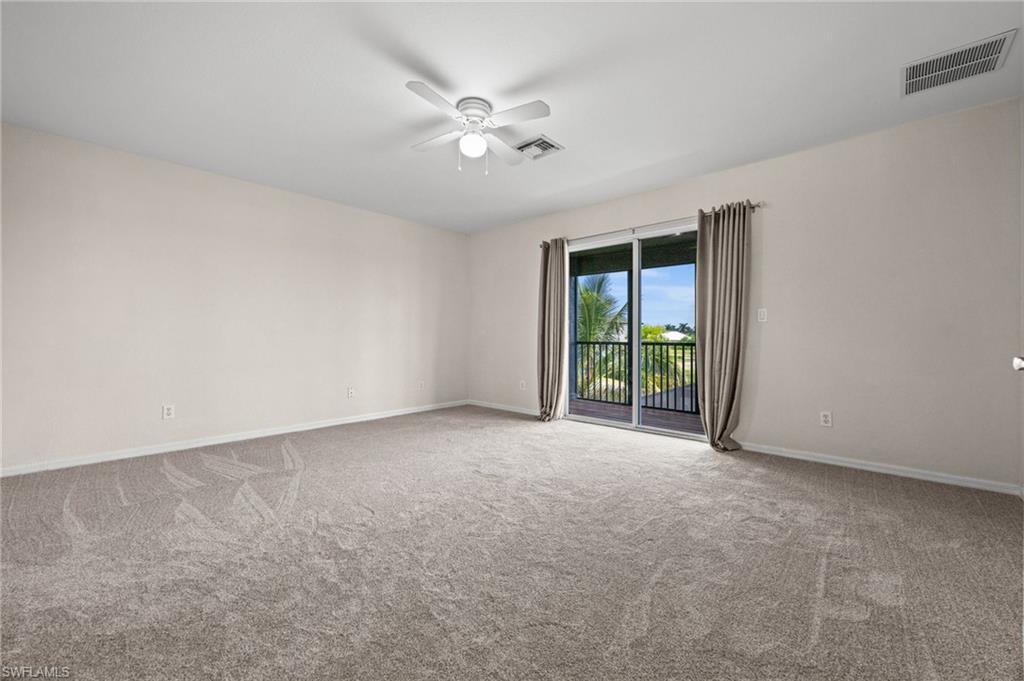 Generously sized upstairs primary bedroom features carpeting, a ceiling fan, and sliding glass doors opening to a private screened balcony. The balcony adds natural light and a separate outdoor retreat overlooking the waterfront surroundings.