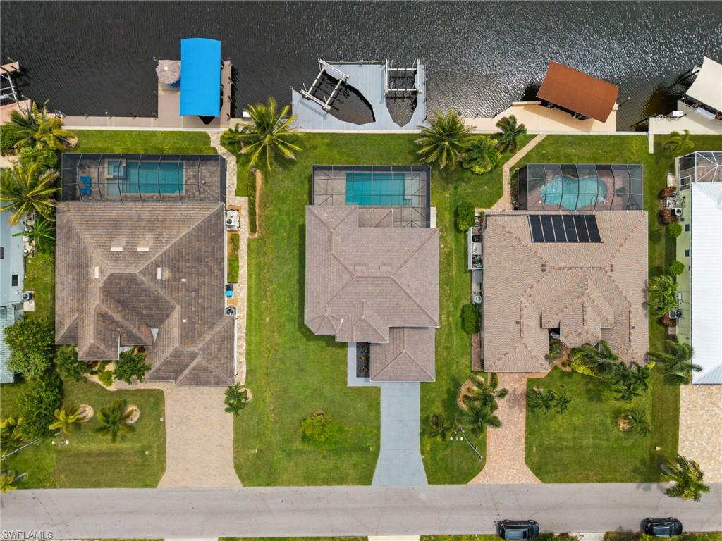 op-down aerial view clearly illustrates the property's layout from street to canal, including the residence, screened pool, backyard, waterfront frontage, custom dock, and neighboring properties.