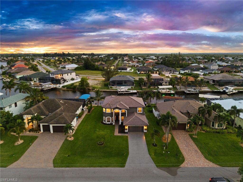 Aerial front view captures the home's two-story architecture, generous yard, driveway, and direct canal location behind the residence. The image provides a clear look at both curb appeal and waterfront positioning.