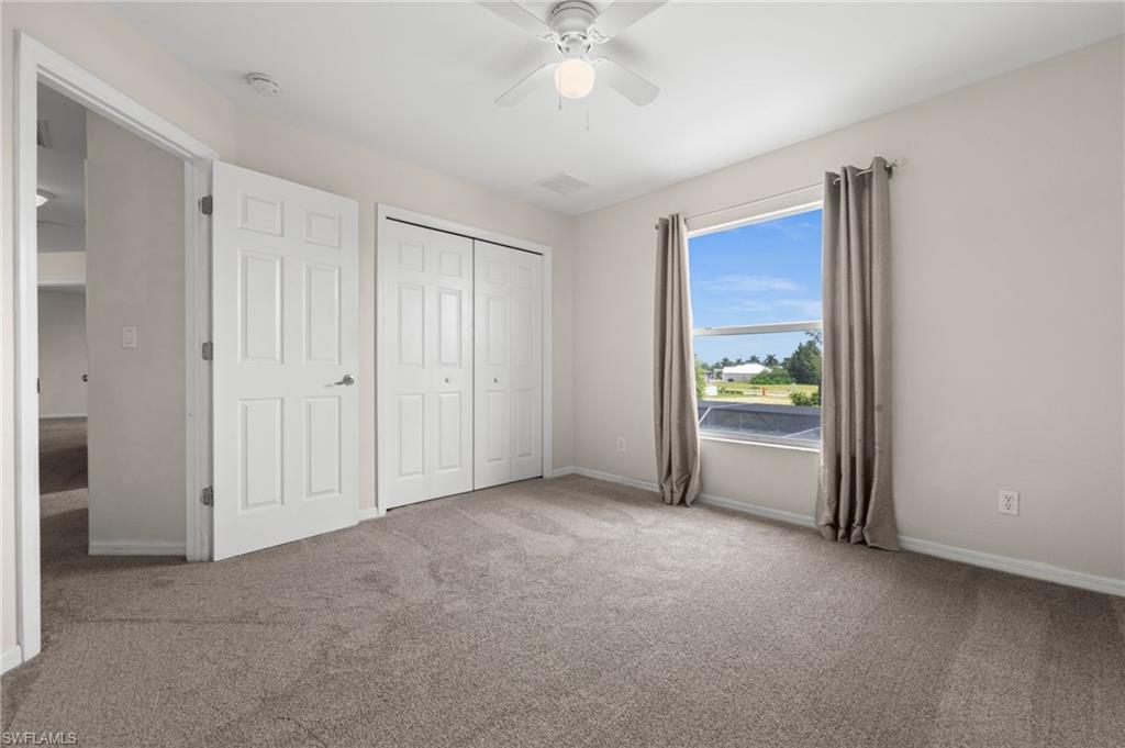 Bright secondary bedroom features carpeting, a ceiling fan, natural light, and closet storage. Neutral finishes make the room easy to personalize for family, guests, or office use.