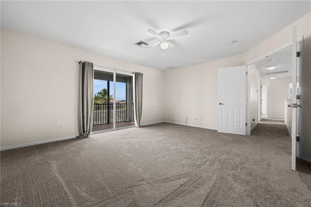 Another view of the spacious primary suite emphasizes the room's size, neutral carpeting, ceiling fan, and direct access to the private screened balcony. The layout provides ample flexibility for a large bedroom furniture arrangement.