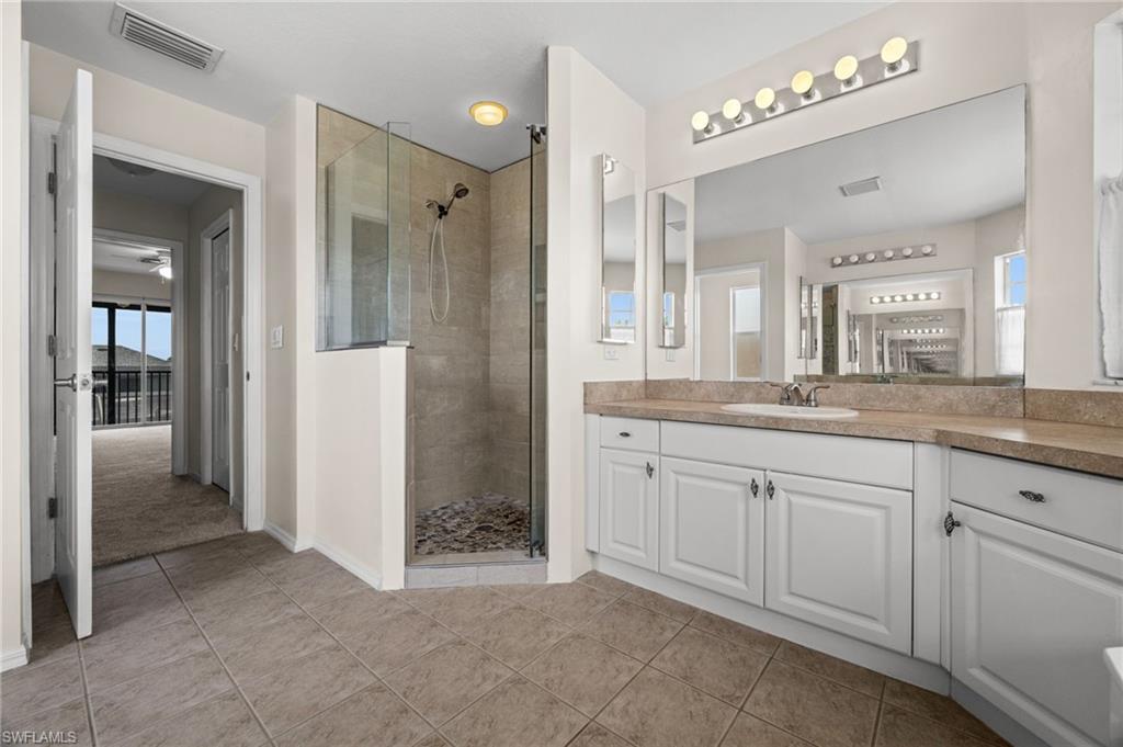 Additional primary-bath view highlights the large vanity area and tiled walk-in shower with frameless glass enclosure. The bathroom's generous footprint creates useful separation between bathing and vanity areas.