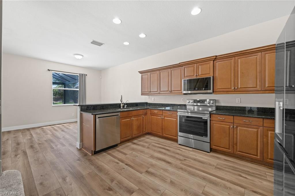 Open kitchen and dining area features extensive cabinetry, black granite countertops, recessed lighting, and stainless steel appliances. The kitchen remains connected to the main living space while offering generous storage and work surfaces.