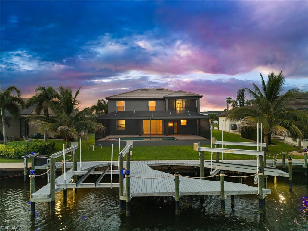 Rear aerial view showcases the screened pool enclosure, expansive lanai, lawn, canal frontage, and substantial private dock. The combination of outdoor living and boating features creates a strong waterfront lifestyle package.
