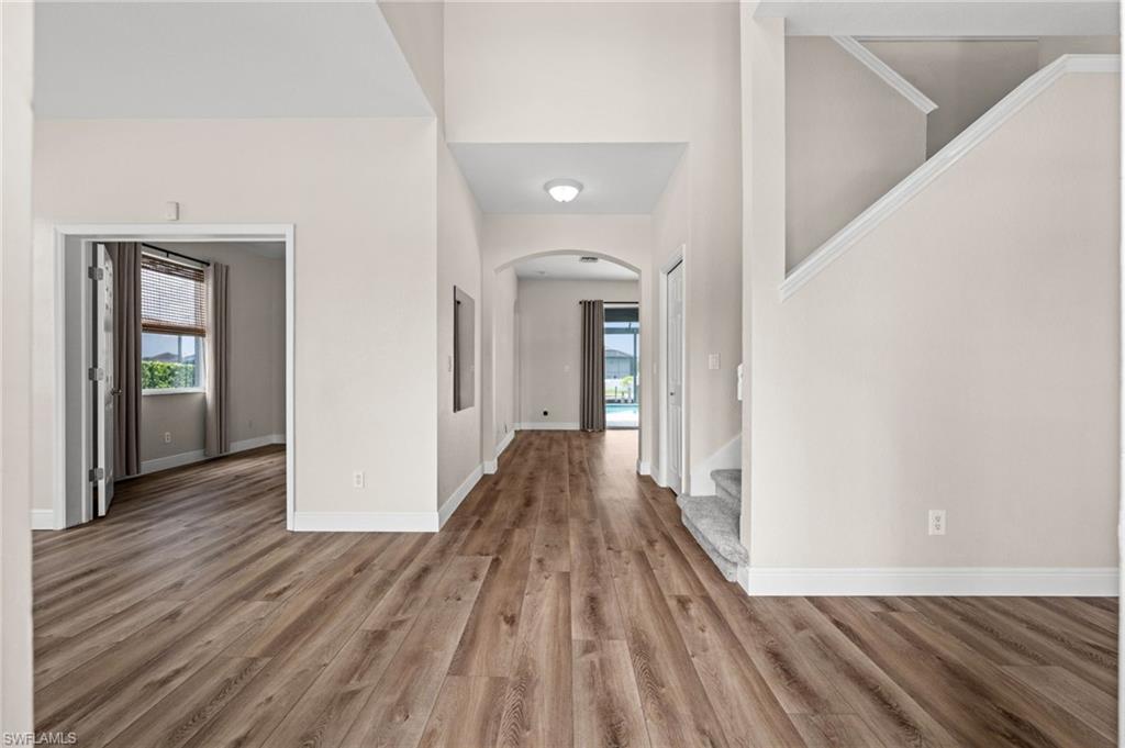 Welcoming main-level interior features tall ceilings, wood-look flooring, an open staircase, and a long sightline toward the pool area. The layout immediately establishes a bright, open connection between the home's interior and outdoor living spaces.