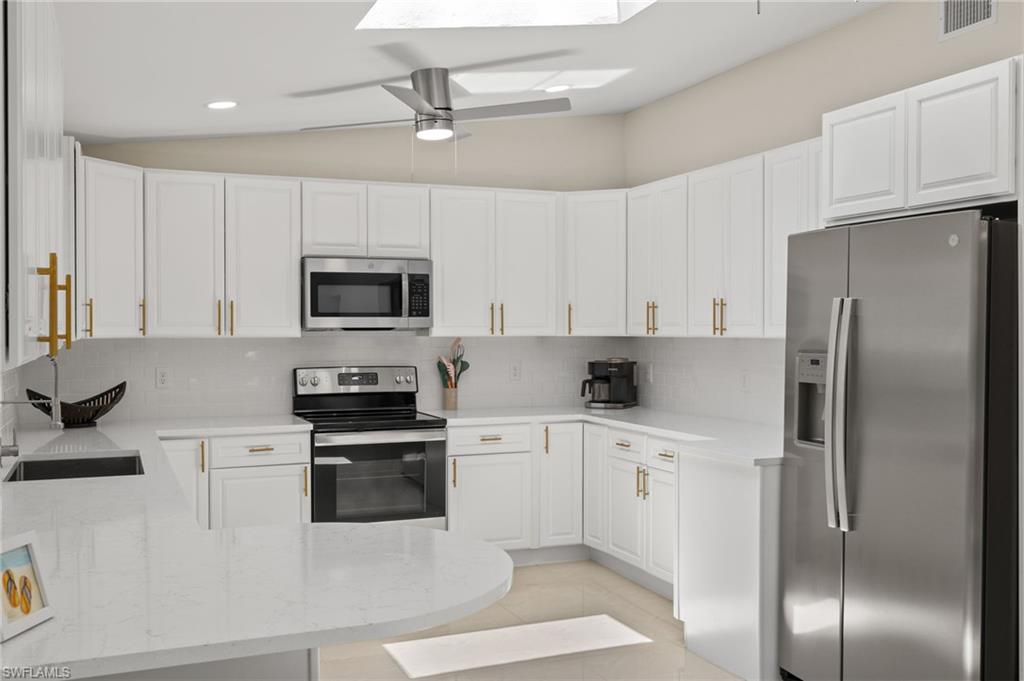 Kitchen with stainless steel appliances, ceiling fan, white cabinetry, light tile floors, and lofted ceiling