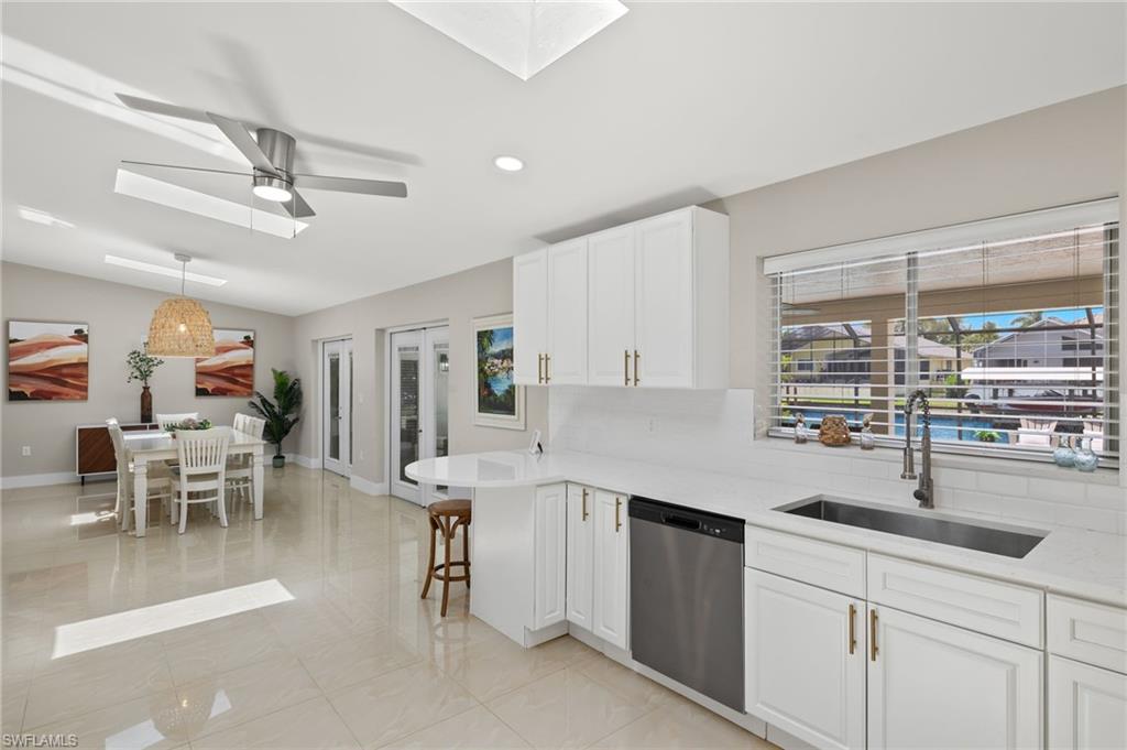 Kitchen with light tile flooring, ceiling fan, stainless steel dishwasher, white cabinets, and sink