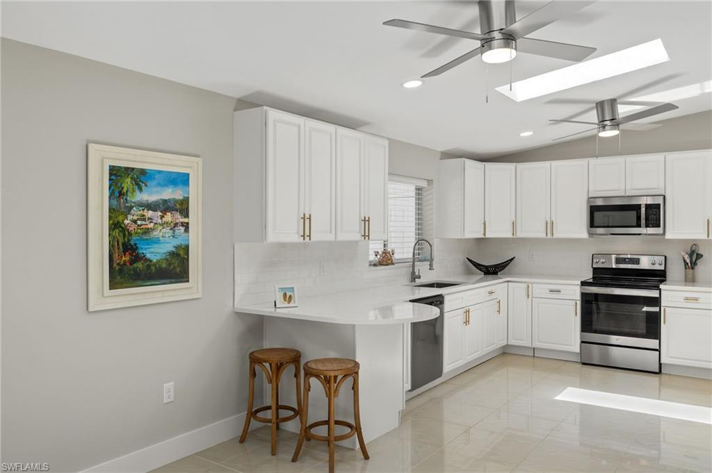 Kitchen featuring appliances with stainless steel finishes, vaulted ceiling with skylight, sink, light tile flooring, and a kitchen bar