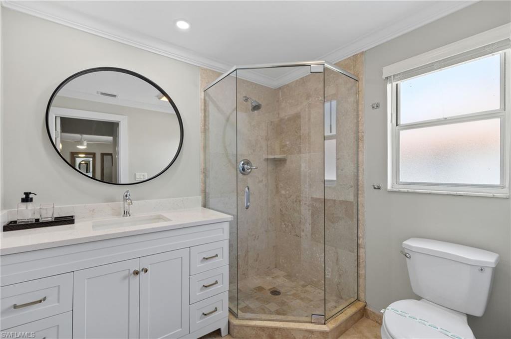 Bathroom with a shower with shower door, crown molding, vanity, and toilet