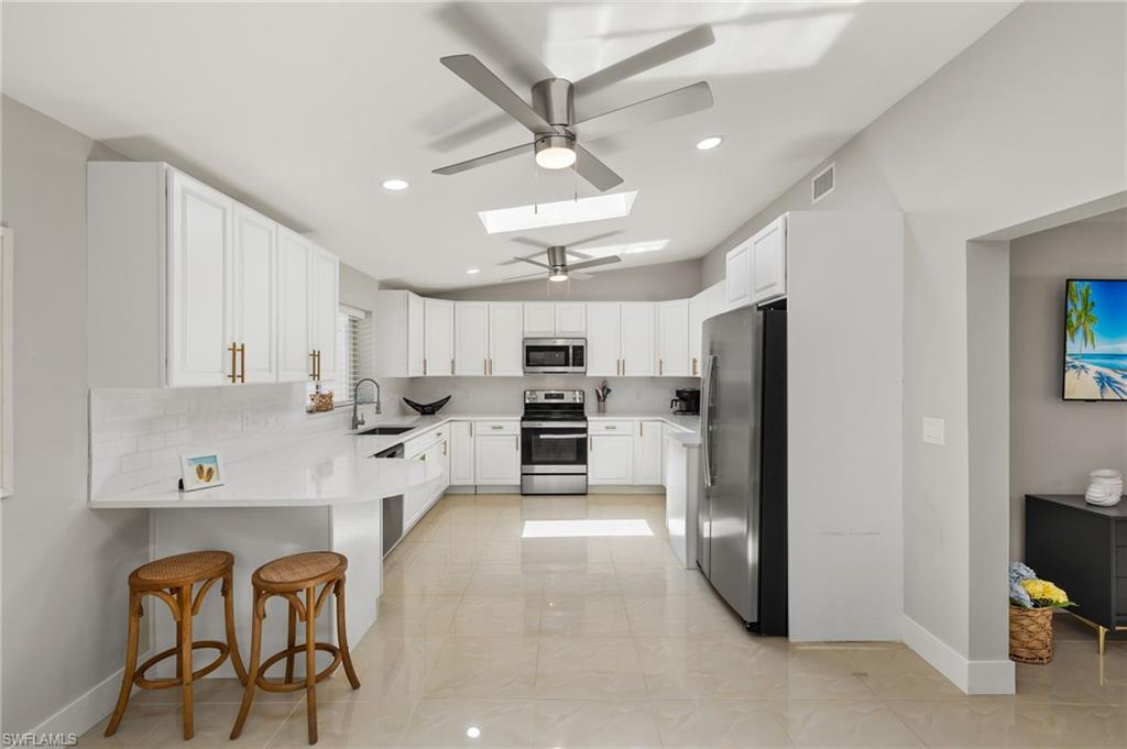 Kitchen featuring appliances with stainless steel finishes, kitchen peninsula, a breakfast bar, sink, and a skylight