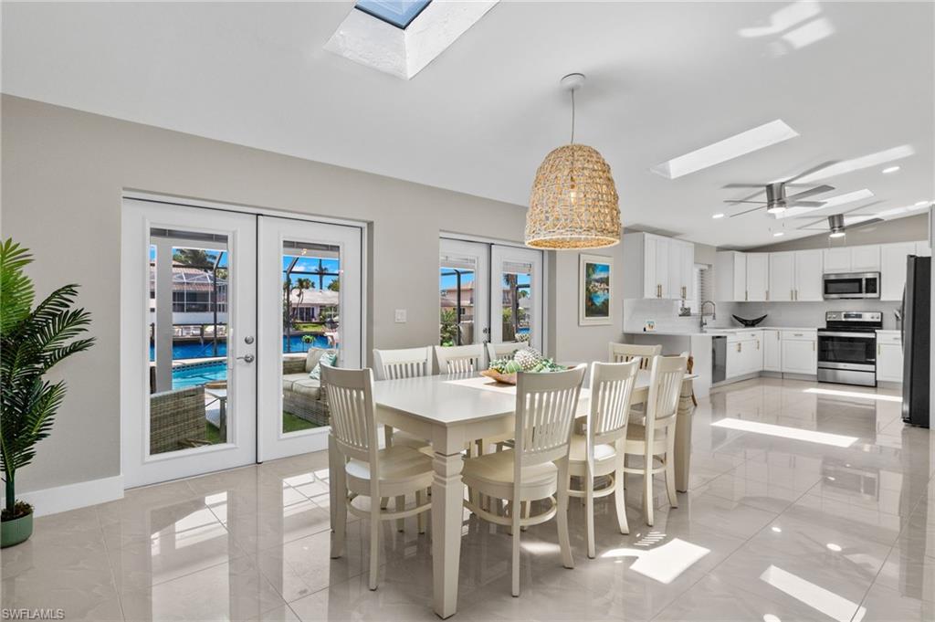 Dining room featuring ceiling fan, light tile flooring, french doors, and a skylight