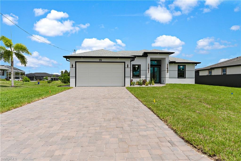 Paver driveway leading to a modern exterior with a two-car garage, black-framed windows, and a prominent front entry