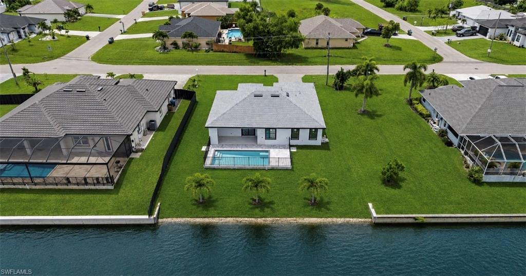 Waterfront property featuring a private pool, screened lanai, manicured lawn, and mature palm trees