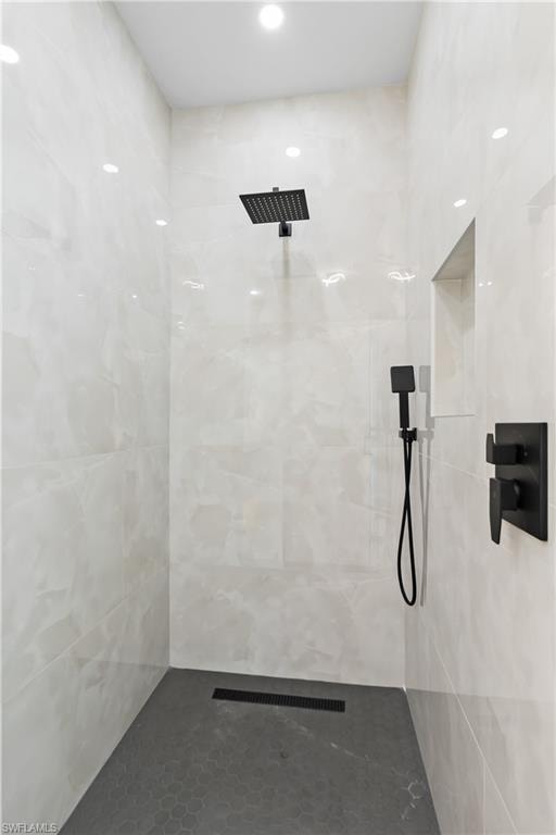 Walk-in shower with full-height wall tiling, recessed lighting, matte black fixtures, and a tiled shower niche