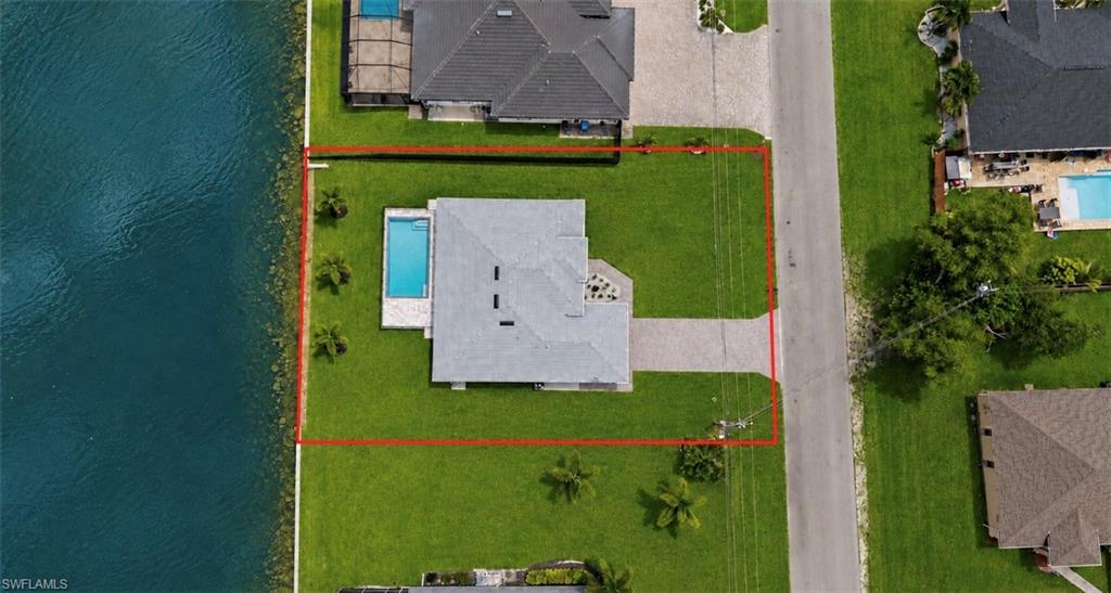 Waterfront property featuring a private swimming pool, expansive green lawn, and a paved driveway