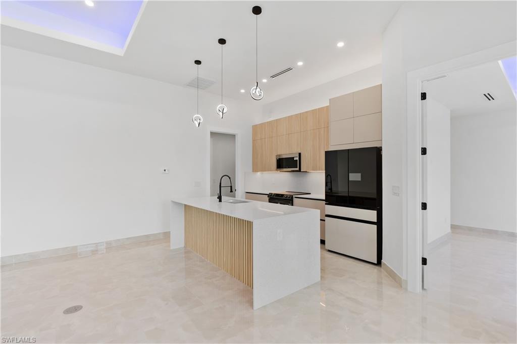 Contemporary kitchen featuring a white quartz island with slatted wood-finish paneling, pendant lighting, built-in stainless steel microwave, and integrated refrigerator