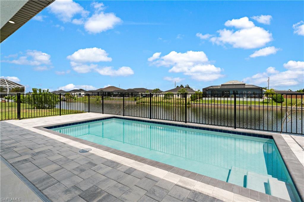 Rectangular swimming pool with integrated steps, surrounded by paver decking, and secured by a black metal fence