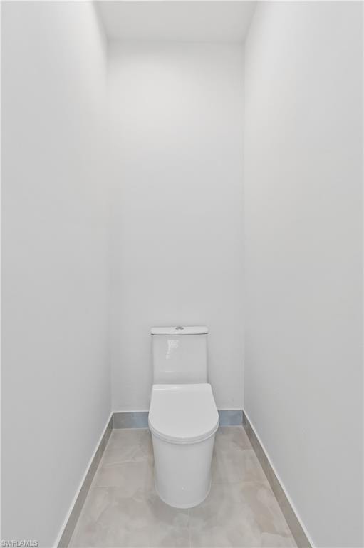 Contemporary water closet featuring a white toilet, tile flooring, and matching tile baseboards