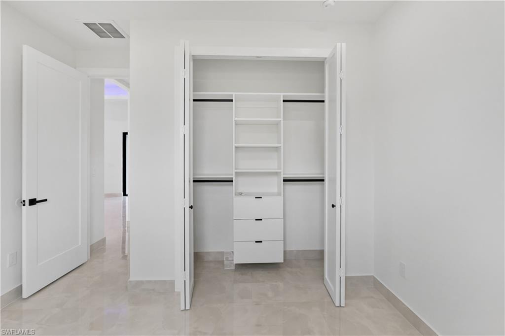 Built-in closet system with shelving and drawers, bifold closet doors, and light-toned tile flooring