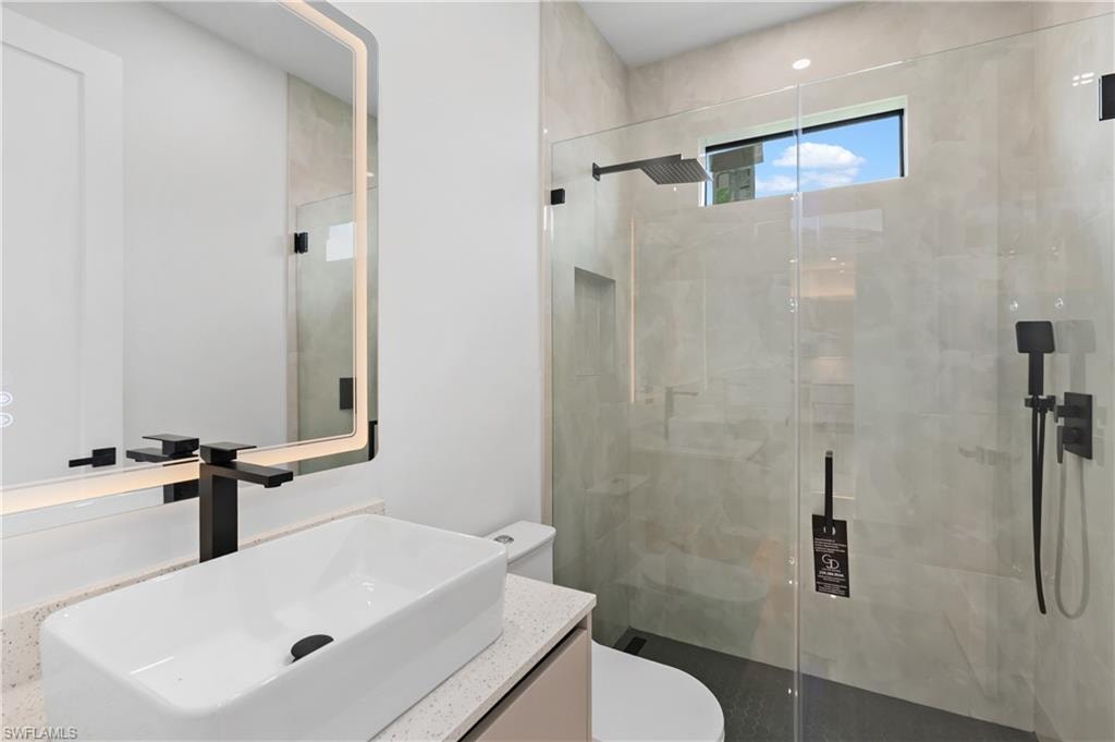 Modern bathroom featuring a rectangular vessel sink, matte black fixtures, an illuminated mirror, a glass-enclosed shower, and a built-in shower niche