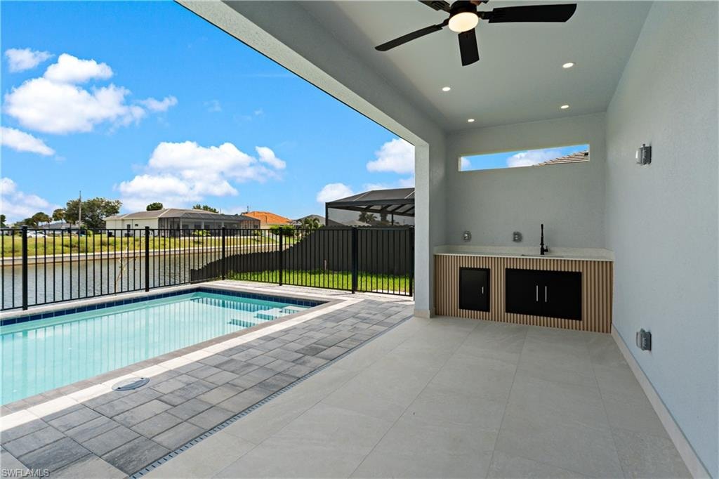Expansive outdoor living area featuring a built-in swimming pool, paved pool deck, and a modern outdoor kitchen with sink